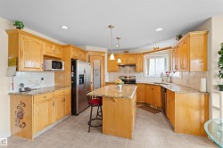 Kitchen featuring wood cabinetry, light granite-style countertops, and a central island with pendant lighting - 