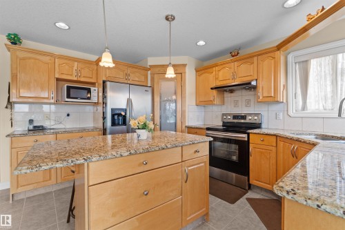 Kitchen featuring wood cabinetry, stainless steel appliances, granite countertops, a center island with a breakfast bar, and recessed lighting - 7622 168A Avenue, Edmonton, AB - Indoor Photo Showing Kitchen