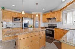 Kitchen featuring wood cabinetry, stainless steel appliances, granite countertops, a center island with a breakfast bar, and recessed lighting - 