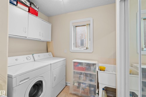 Dedicated laundry space featuring a white utility sink, upper cabinetry, and a window for natural light - 7622 168A Avenue, Edmonton, AB - Indoor Photo Showing Laundry Room