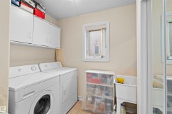 Dedicated laundry space featuring a white utility sink, upper cabinetry, and a window for natural light - 