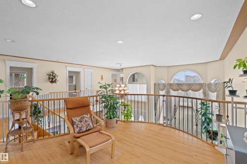 Curved balcony overlooking lower level featuring wood-finish flooring, wrought iron balusters, recessed lighting, and arched windows - 7622 168A Avenue, Edmonton, AB - Indoor Photo Showing Other Room
