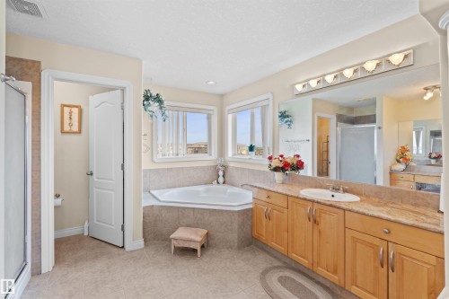 Bathroom featuring a corner soaking tub, dual windows, and a vanity with a drop-in sink and light wood cabinetry - 7622 168A Avenue, Edmonton, AB - Indoor Photo Showing Bathroom