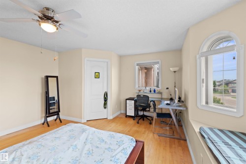 Bedroom featuring wood-finish flooring, a ceiling fan with integrated lighting, an arched window, and a built-in window bench - 7622 168A Avenue, Edmonton, AB - Indoor Photo Showing Bedroom