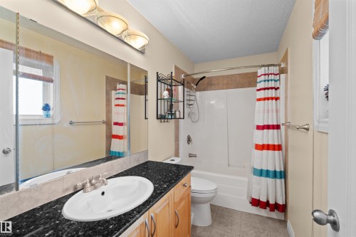 Bathroom featuring a vanity with a dark speckled countertop, an integrated sink, and light wood cabinetry - 7622 168A Avenue, Edmonton, AB - Indoor Photo Showing Bathroom