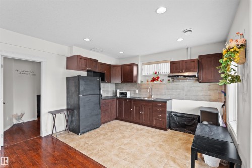 Kitchen featuring wood-finish cabinetry, dark countertops, a tile backsplash, and a stainless steel sink - 7622 168A Avenue, Edmonton, AB - Indoor Photo Showing Kitchen With Double Sink