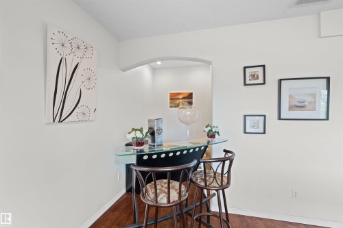 Compact bar area featuring a glass countertop and rich wood-finish flooring - 7622 168A Avenue, Edmonton, AB - Indoor