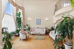 Two-story living area featuring light wood-finish flooring, a grand two-story window with drapery, and a curved second-story balcony with wrought iron railing - 