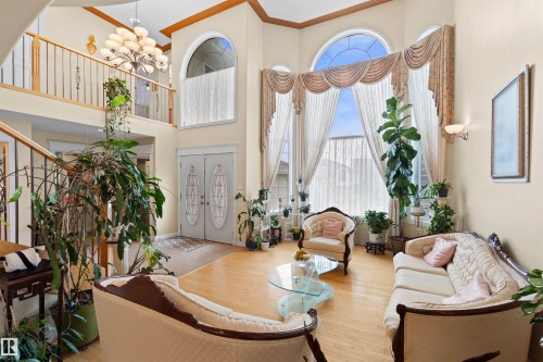 Two-story foyer featuring double entry doors with decorative glass inserts, hardwood flooring, an open balcony, and a prominent chandelier - 7622 168A Avenue, Edmonton, AB - Indoor