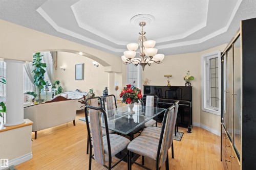Formal dining area featuring a tray ceiling with a central chandelier, wood-finish flooring, and an arched entry to an additional living space - 7622 168A Avenue, Edmonton, AB - Indoor Photo Showing Dining Room