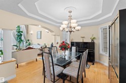 Formal dining area featuring a tray ceiling with a central chandelier, wood-finish flooring, and an arched entry to an additional living space - 