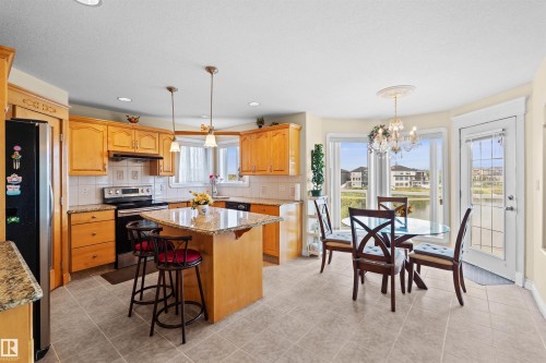 Kitchen and dining area featuring light wood cabinetry, stone countertops, stainless steel appliances, and a central island with pendant lighting - 7622 168A Avenue, Edmonton, AB - Indoor