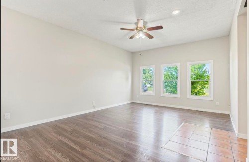 Spacious room featuring wood-finish flooring, light-toned wall paint, and white baseboards - 10211 95 Ave, Morinville, AB - Indoor Photo Showing Other Room