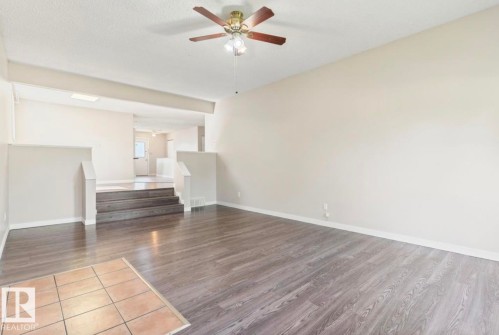 Spacious room featuring wood-finish flooring, a neutral color palette, a ceiling fan with integrated lighting, and a skylight for natural illumination - 10211 95 Ave, Morinville, AB - Indoor Photo Showing Other Room