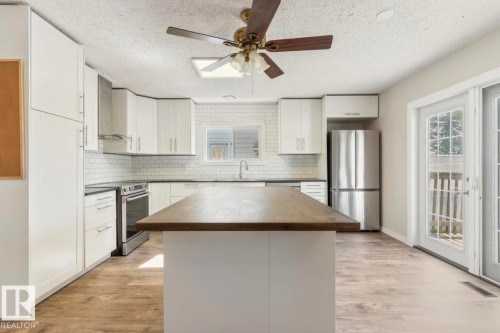 Modern kitchen featuring a large central island with wood-finish countertop, white cabinetry with contemporary hardware, stainless steel appliances, and a white subway tile backsplash - 10211 95 Ave, Morinville, AB - Indoor Photo Showing Kitchen With Stainless Steel Kitchen With Upgraded Kitchen