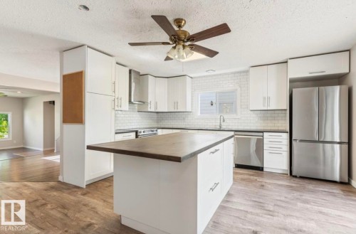 Kitchen featuring wood-finish flooring, white cabinetry, a central island with a contrasting countertop, stainless steel appliances, and a white subway tile backsplash - 10211 95 Ave, Morinville, AB - Indoor Photo Showing Kitchen With Stainless Steel Kitchen With Upgraded Kitchen