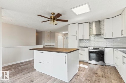 Kitchen featuring a central island with wood-finish countertop, white cabinetry with contemporary hardware, stainless steel appliances, subway tile backsplash, and wood-finish flooring - 10211 95 Ave, Morinville, AB - Indoor Photo Showing Kitchen With Upgraded Kitchen