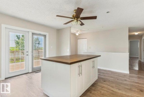 Kitchen island with a rich wood-finish countertop, white cabinetry, and brushed nickel hardware - 10211 95 Ave, Morinville, AB - Indoor Photo Showing Other Room