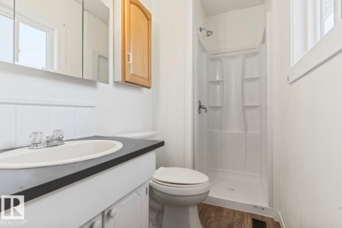 Bathroom featuring a single vanity with a white basin and dark countertop, a mirrored medicine cabinet, a built-in shower stall, and a window providing natural light - 10211 95 Ave, Morinville, AB - Indoor Photo Showing Bathroom