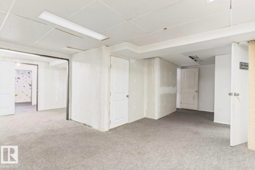 Spacious interior area featuring light gray carpeting, white panel doors, and a drop ceiling with integrated fluorescent lighting - 10211 95 Ave, Morinville, AB - Indoor