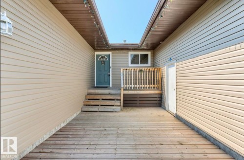 Entryway featuring a wood-finish deck, light beige horizontal siding, a blue arched-paneled door, and exposed wood-finish steps - 10211 95 Ave, Morinville, AB - Outdoor With Exterior