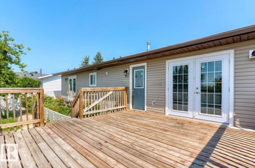 Expansive exterior wood deck featuring a full-width railing system, direct access via white French doors, and an additional exterior door - 10211 95 Ave, Morinville, AB - Outdoor With Deck Patio Veranda With Exterior