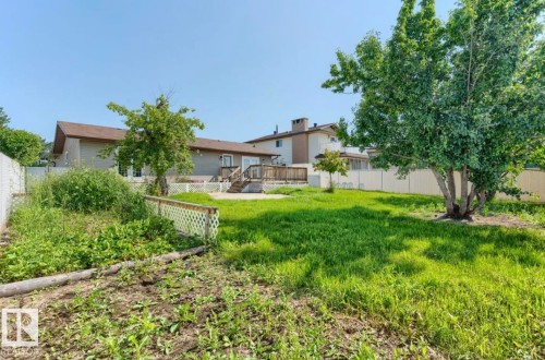 Expansive rear yard featuring mature trees, a wooden deck with lattice railing, and a ground-level patio - 10211 95 Ave, Morinville, AB - Outdoor