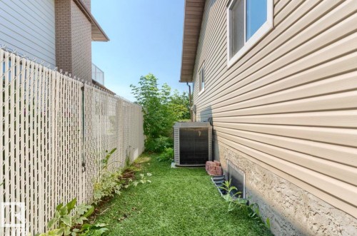Side yard featuring a chain-link fence with privacy slats, green lawn, and a visible air conditioning unit - 10211 95 Ave, Morinville, AB - Outdoor With Exterior