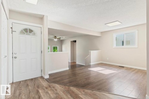 Entryway featuring a decorative transom window above a paneled door, wood-finish flooring, neutral wall paint, and a rectangular ceiling light fixture - 10211 95 Ave, Morinville, AB - Indoor Photo Showing Other Room