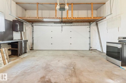 Garage space featuring a concrete floor, overhead storage structure, and a roll-up door - 10211 95 Ave, Morinville, AB - Indoor Photo Showing Garage