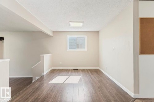 Spacious interior featuring wood-finish flooring, neutral wall tones, white trim, and a contemporary ceiling light fixture - 10211 95 Ave, Morinville, AB - Indoor Photo Showing Other Room