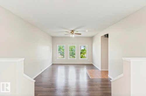 Spacious room featuring three large windows, wood-finish flooring, a ceiling fan, light neutral wall tones, and white trim - 10211 95 Ave, Morinville, AB - Indoor Photo Showing Other Room