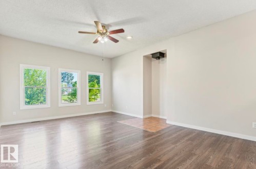 Spacious room featuring three large windows, wood-finish flooring, a ceiling fan with integrated lighting, and neutral wall tones - 10211 95 Ave, Morinville, AB - Indoor Photo Showing Other Room