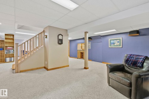 Finished lower level featuring light-colored carpeting, a natural wood staircase with balusters, built-in shelving, a recessed lighting system, and a built-in bar area - 7306 21 Avenue Nw, Edmonton, AB - Indoor Photo Showing Basement