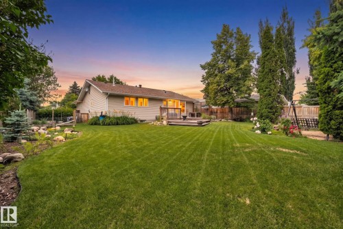 Expansive landscaped backyard featuring a tiered wooden deck, mature trees, manicured lawn, and a stone-lined garden bed - 7306 21 Avenue Nw, Edmonton, AB - Outdoor