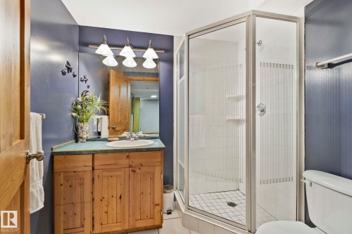 Bathroom featuring a corner shower enclosure, a wood-finish vanity with an integrated sink, a rectangular mirror, overhead vanity lighting, and blue-painted walls - 7306 21 Avenue Nw, Edmonton, AB - Indoor Photo Showing Bathroom