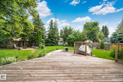 Spacious backyard featuring a large wooden deck with railings, an expansive lawn, mature trees, a fire pit area with stone paving, and a privacy fence - 7306 21 Avenue Nw, Edmonton, AB - Outdoor With Deck Patio Veranda