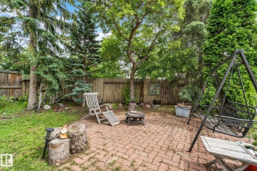 Paved brick patio with a central fire pit feature, surrounded by mature trees and a wood privacy fence - 7306 21 Avenue Nw, Edmonton, AB - Outdoor