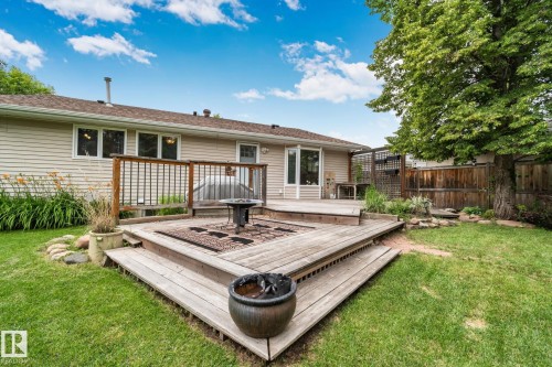 Tiered wood deck with integrated fire pit feature, surrounded by a manicured lawn and mature perimeter trees - 7306 21 Avenue Nw, Edmonton, AB - Outdoor