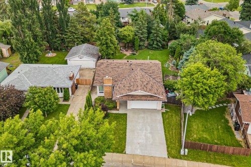 Single-family residence featuring a prominent brown shingle roof, attached front-facing garage with a concrete driveway, and a fenced backyard with mature trees - 7306 21 Avenue Nw, Edmonton, AB - Outdoor