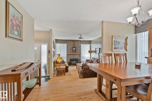 Open-concept interior featuring wood-finish flooring, a dining area with a wood table, and a living area with a brick fireplace - 7306 21 Avenue Nw, Edmonton, AB - Indoor Photo Showing Dining Room With Fireplace