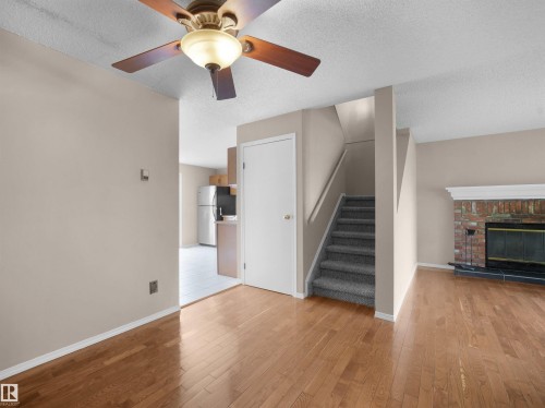 Living area featuring wood-finish flooring, a ceiling fan with integrated lighting, and a brick fireplace with a white mantel - 3509 43A Avenue Nw, Edmonton, AB - Indoor Photo Showing Other Room With Fireplace