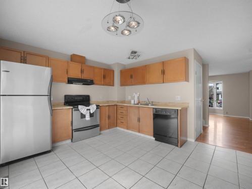 Kitchen featuring light wood cabinetry, a stainless steel refrigerator, a black range with an overhead vent, and a black dishwasher - 3509 43A Avenue Nw, Edmonton, AB - Indoor Photo Showing Kitchen With Double Sink