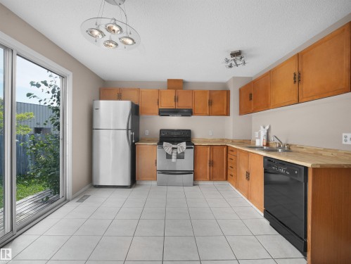Kitchen featuring wood cabinetry, stainless steel refrigerator, black dishwasher, black range, and white tiled flooring - 3509 43A Avenue Nw, Edmonton, AB - Indoor Photo Showing Kitchen With Double Sink