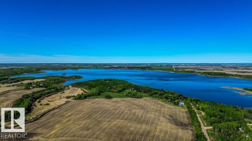 Expansive aerial perspective showcasing a vast body of water, surrounded by lush green tree lines and agricultural land - 705 59128 Rng Rd 95, Rural St. Paul County, AB 