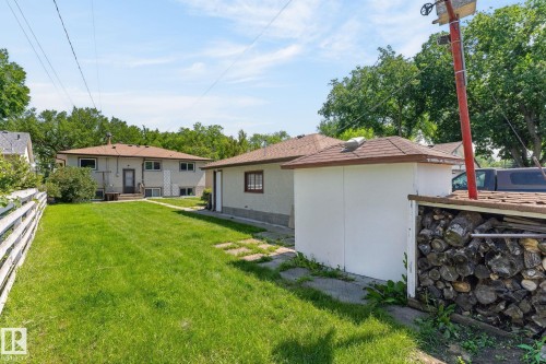 Expansive backyard featuring a manicured lawn, a detached garage with brown trim, and a separate storage structure with a shingle roof - 12908 104 Street Nw, Edmonton, AB - Outdoor