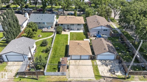 Rear exterior featuring a spacious green lawn, mature trees, a wooden deck, and a detached two-car garage with a brown shingle roof - 12908 104 Street Nw, Edmonton, AB - Outdoor
