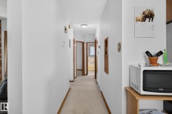 Carpeted hallway with white walls and wood-finish trim, featuring multiple wood-finish doors - 