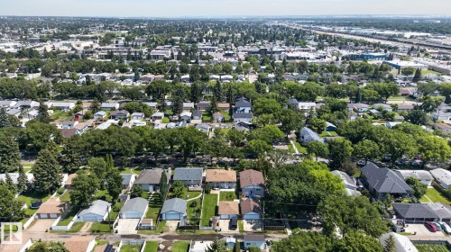 Expansive aerial perspective showcasing a residential neighborhood with numerous detached homes, mature trees, and a distant commercial/industrial area - 12908 104 Street Nw, Edmonton, AB - Outdoor With View