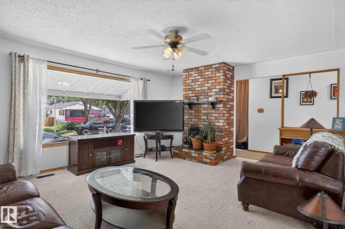Living area featuring a brick fireplace, ceiling fan, and large picture window - 12908 104 Street Nw, Edmonton, AB - Indoor Photo Showing Living Room With Fireplace